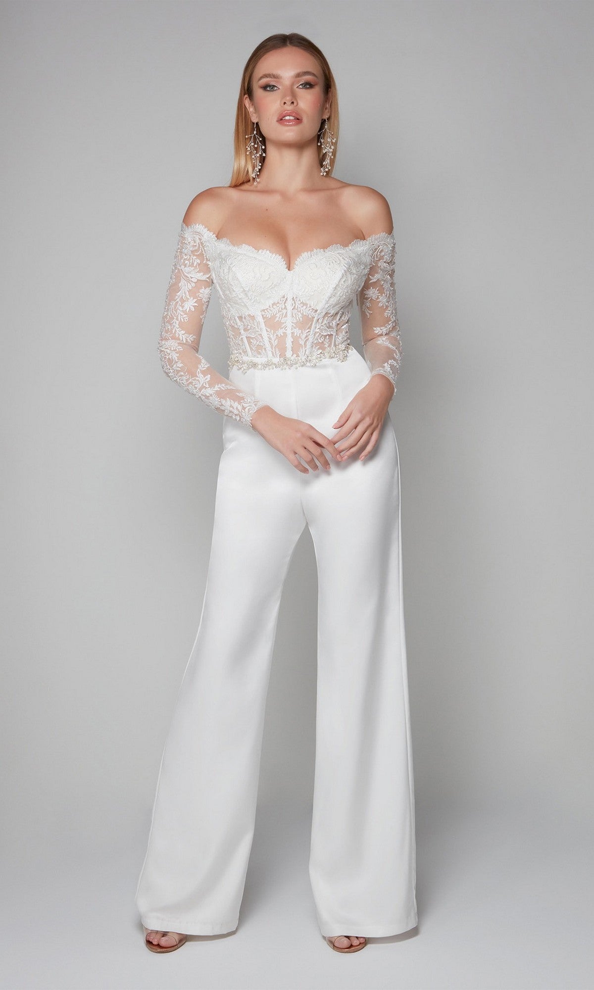 A woman wears the Long Formal Jumpsuit: Alyce 70018 with a white lace embroidery bodice, sheer long sleeves, and wide-leg pants, posing against a light gray background.